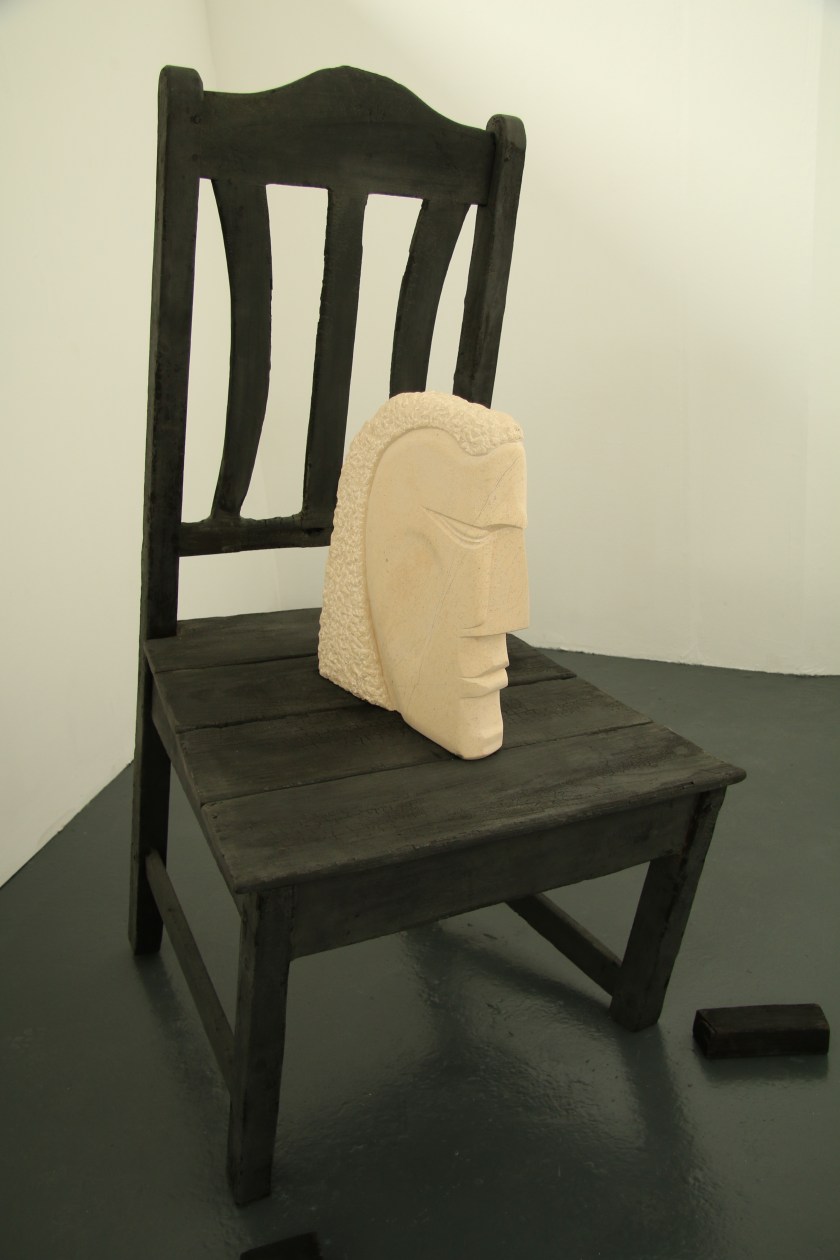This oversize chair has been burnt to represent the passage of time and the stone head is a stylised representation of us as human beings